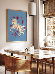 Cream unicorn with red horn and mane prancing among red stars on a light blue background, in a styled room mockup
