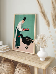 Illustrative print of person in chef's hat holding tray for black duck with red beak on teal, in an alternate framed mockup