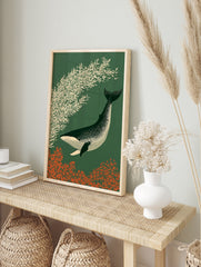 Stylized illustration of a speckled whale swimming past cream foliage on a dark green, in an alternate framed mockup