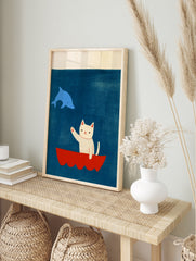 Illustrative art print featuring a white cat waving from a red boat at a blue dolphin against, in an alternate framed mockup