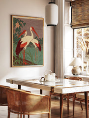 Two white cranes with red heads and wing tips standing in green water with foliage and pink flowers, in a styled room mockup
