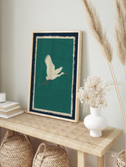 Illustrative white egret flying right against a teal background with navy and cream borders, in an alternate framed mockup