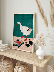 Illustrative print of a large white goose walking, three black ducks, and a tray of food on a, in an alternate framed mockup