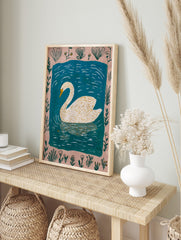 Illustrative white swan with yellow beak swimming in blue water, framed by a pale pink, in an alternate framed mockup