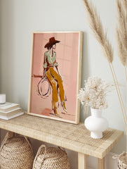 Illustrative print of woman in wide hat and ochre trousers against a pink background, in an alternate framed mockup