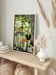 Illustrative woodland art print with large mushrooms, a black squirrel, white plants, and, in an alternate framed mockup