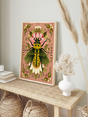 Ornate yellow beetle illustration with green wings and black spots, surrounded by pink and, in an alternate framed mockup