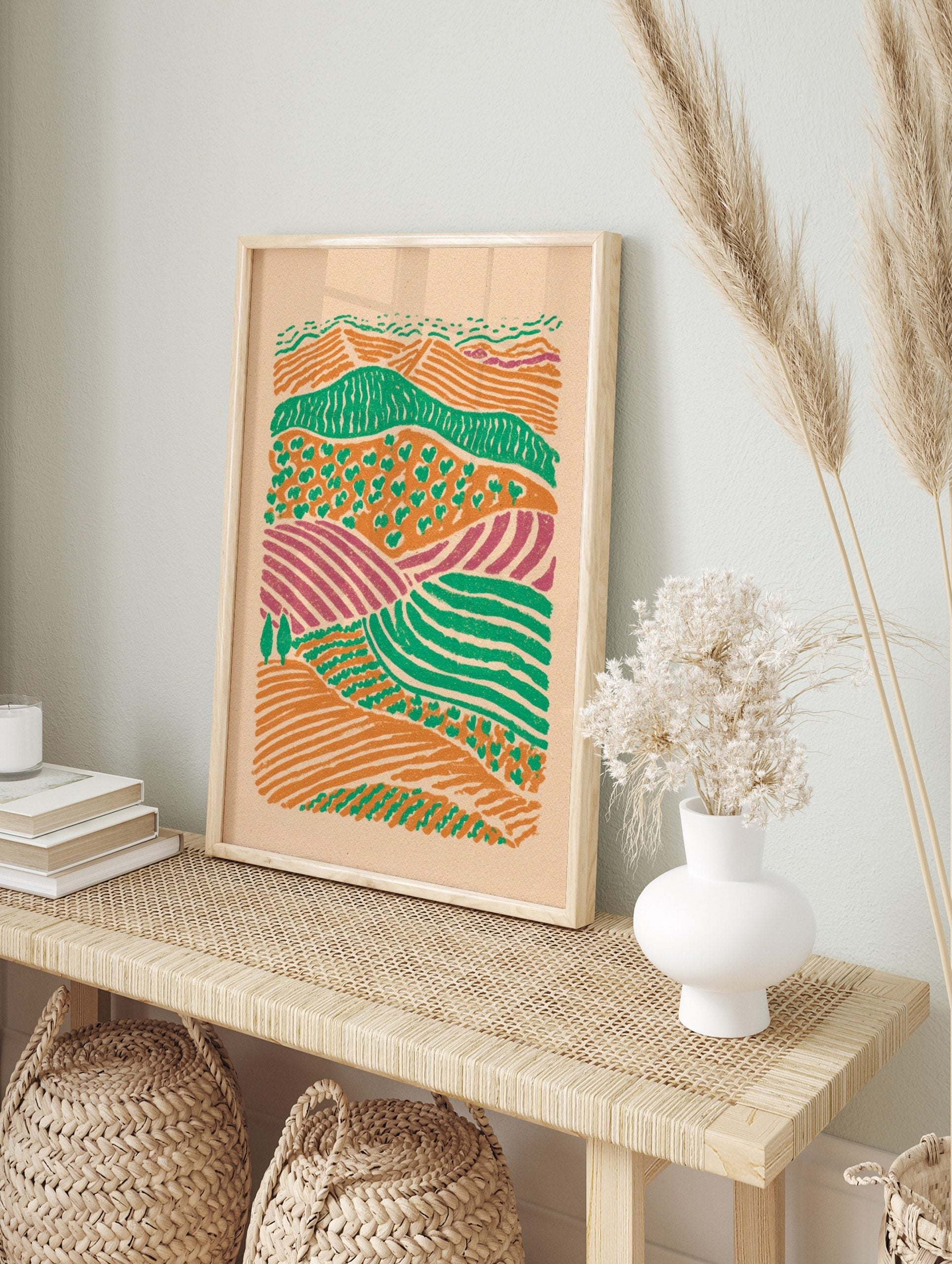 Illustrative abstract landscape print of layered farm fields in orange, green, and purple, in an alternate framed mockup