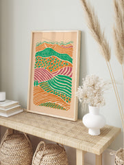 Illustrative abstract landscape print of layered farm fields in orange, green, and purple, in an alternate framed mockup