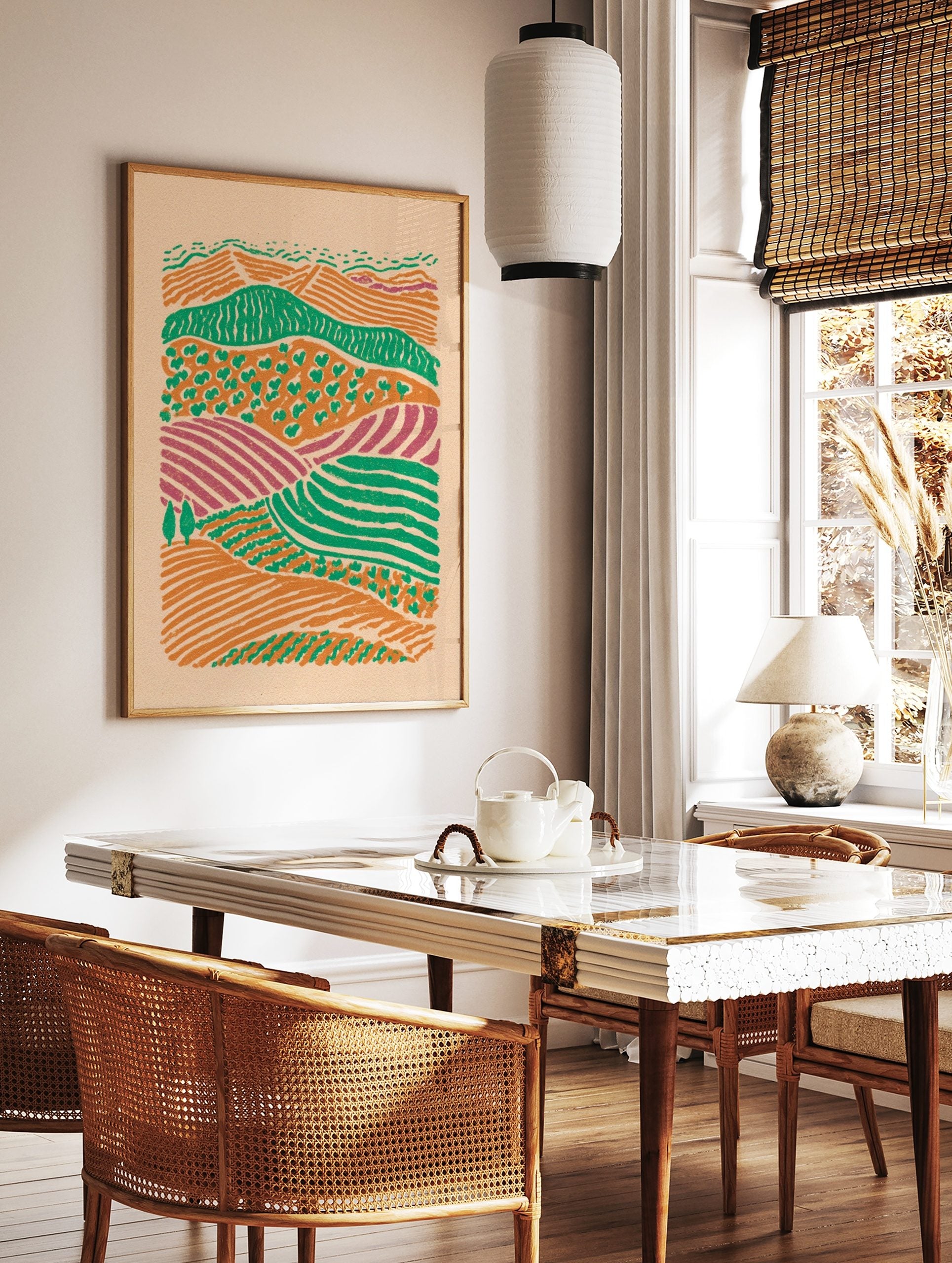 Illustrative abstract landscape print of layered farm fields in orange, green, and purple hues with, in a styled room mockup
