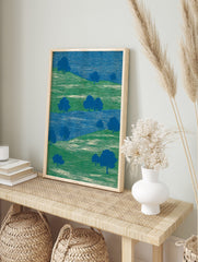 Abstract landscape art print with green rolling hills, blue trees, and a blue river, in an alternate framed mockup