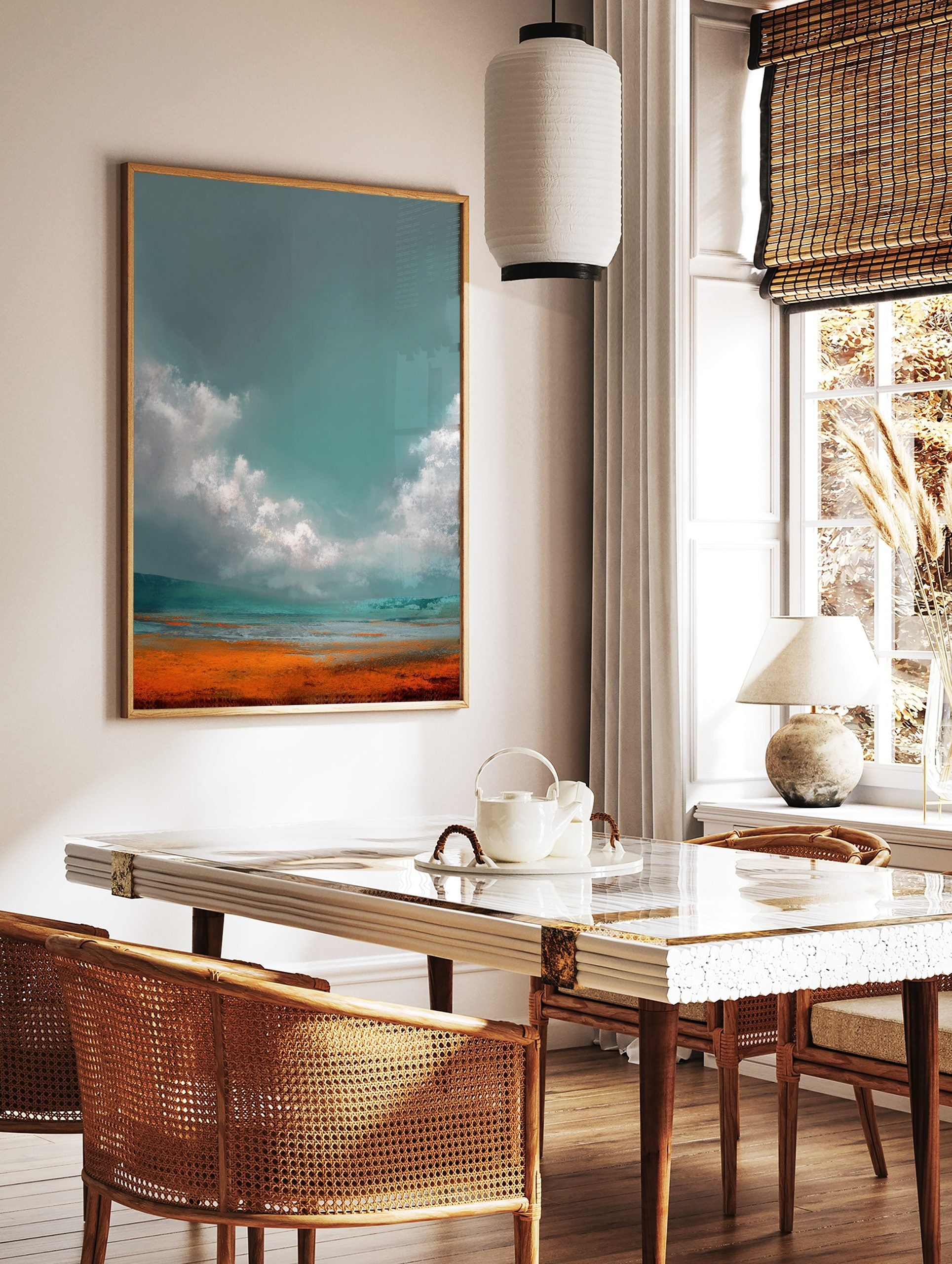 Abstract landscape art print with teal-grey sky, white clouds, and vibrant orange-blue ground, in a styled room mockup