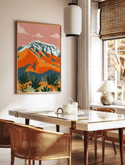 Abstract mountain landscape print with snow-capped peak, orange hills, and green foliage under a, in a styled room mockup