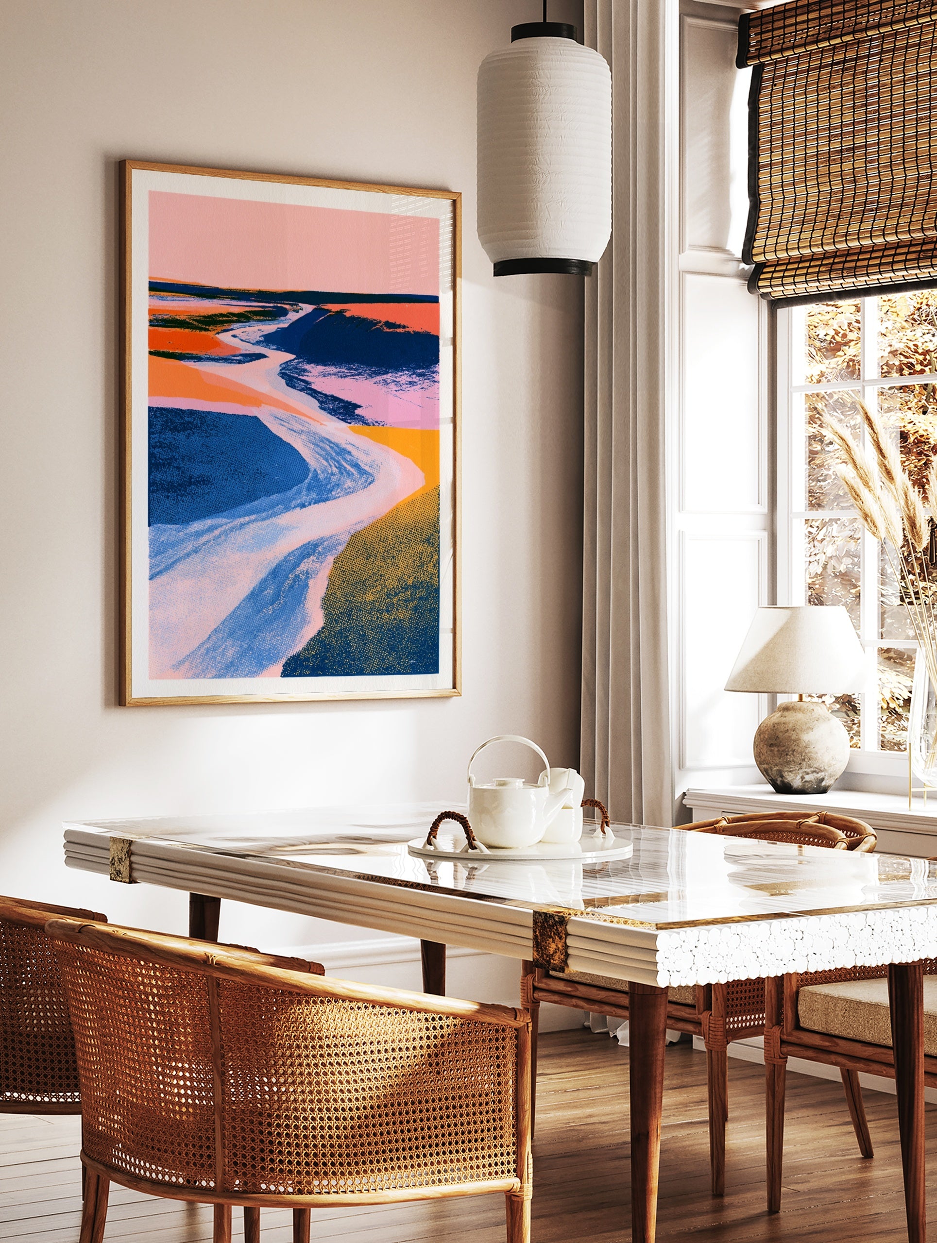 Abstract landscape wall art with a winding river, pink sky, and textured blue and orange fields in, in a styled room mockup