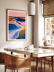 Abstract landscape wall art with a winding river, pink sky, and textured blue and orange fields in, in a styled room mockup