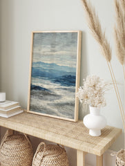 Abstract seascape painting with blue mountains, deep blue ocean, and textured white waves, in an alternate framed mockup