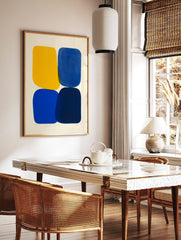 Abstract art print with four rounded shapes in yellow, blue, and navy on an off-white background, in a styled room mockup