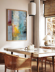 Abstract textured wall art with vertical blocks of red, yellow, blue, and grey paint on a canvas, in a styled room mockup