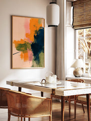 Abstract wall art with layered brushstrokes in orange, navy, olive green, and pink on a pale peach, in a styled room mockup