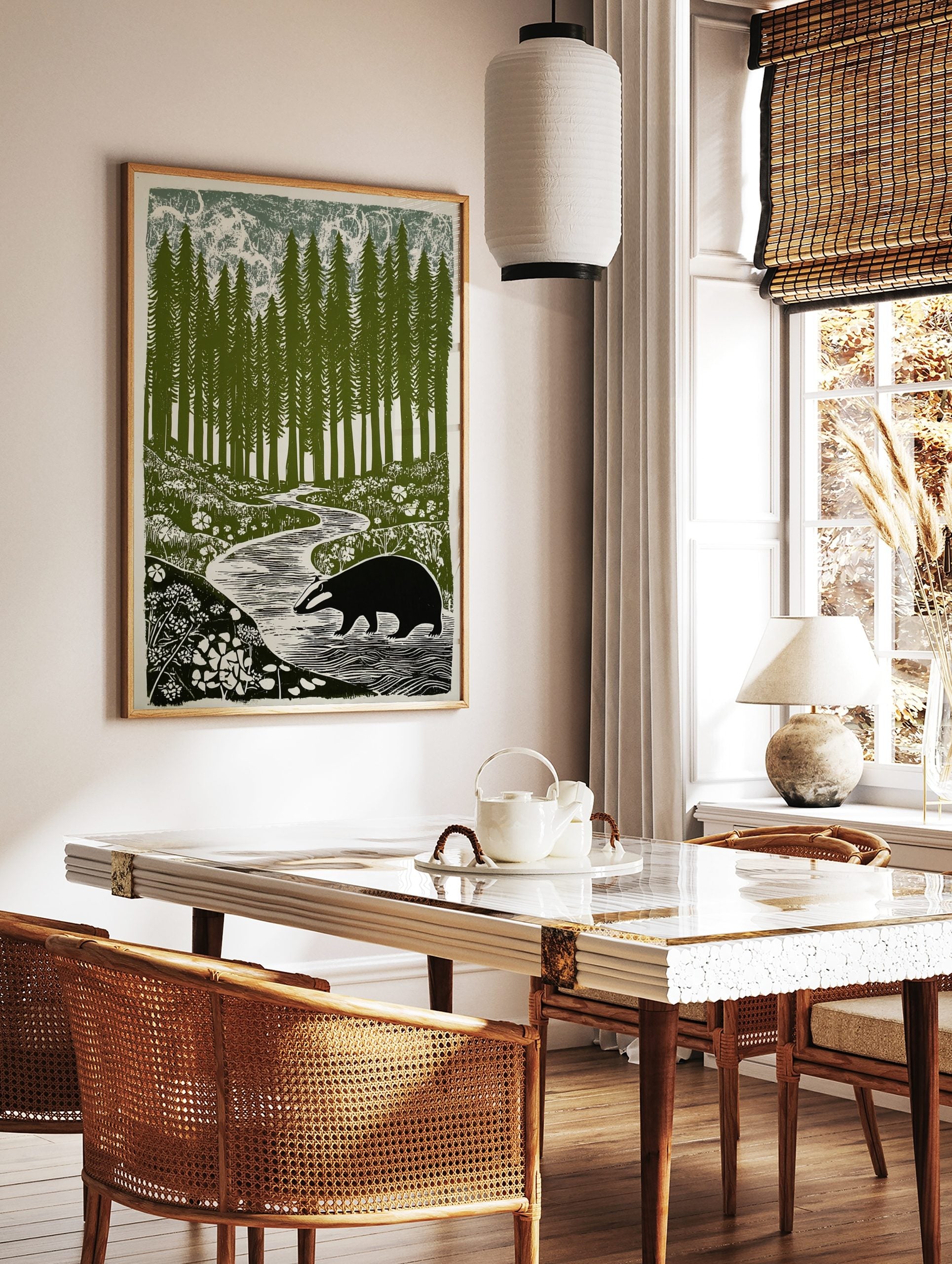 Linocut-style print of a badger walking by a winding river in a forest of tall pine trees and, in a styled room mockup