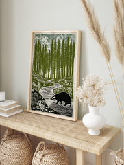 Illustrative print of a badger walking by a winding stream in a forest of tall green trees, in an alternate framed mockup
