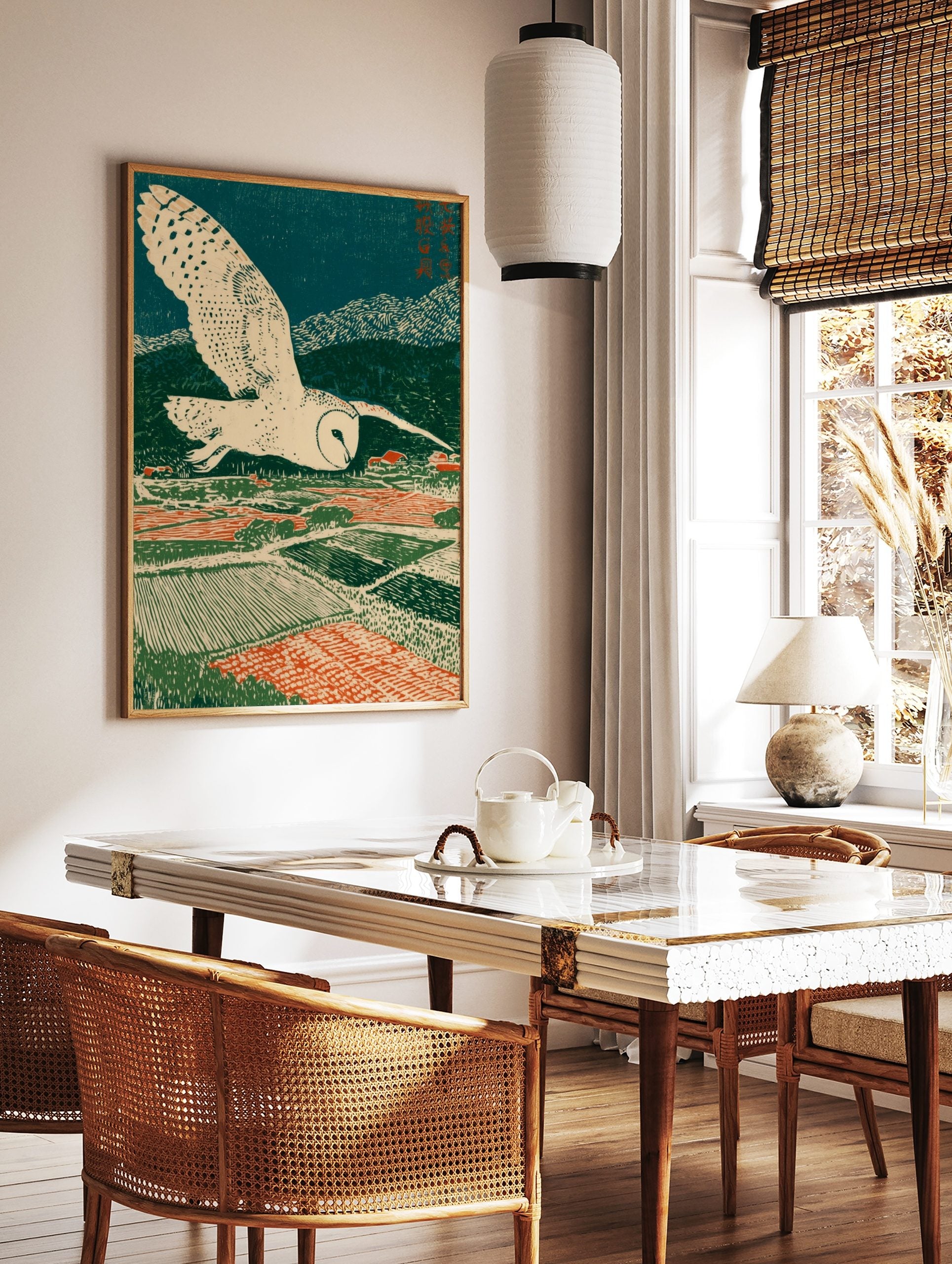 Stylised barn owl flying over patterned green and red fields with a village under a dark blue sky, in a styled room mockup