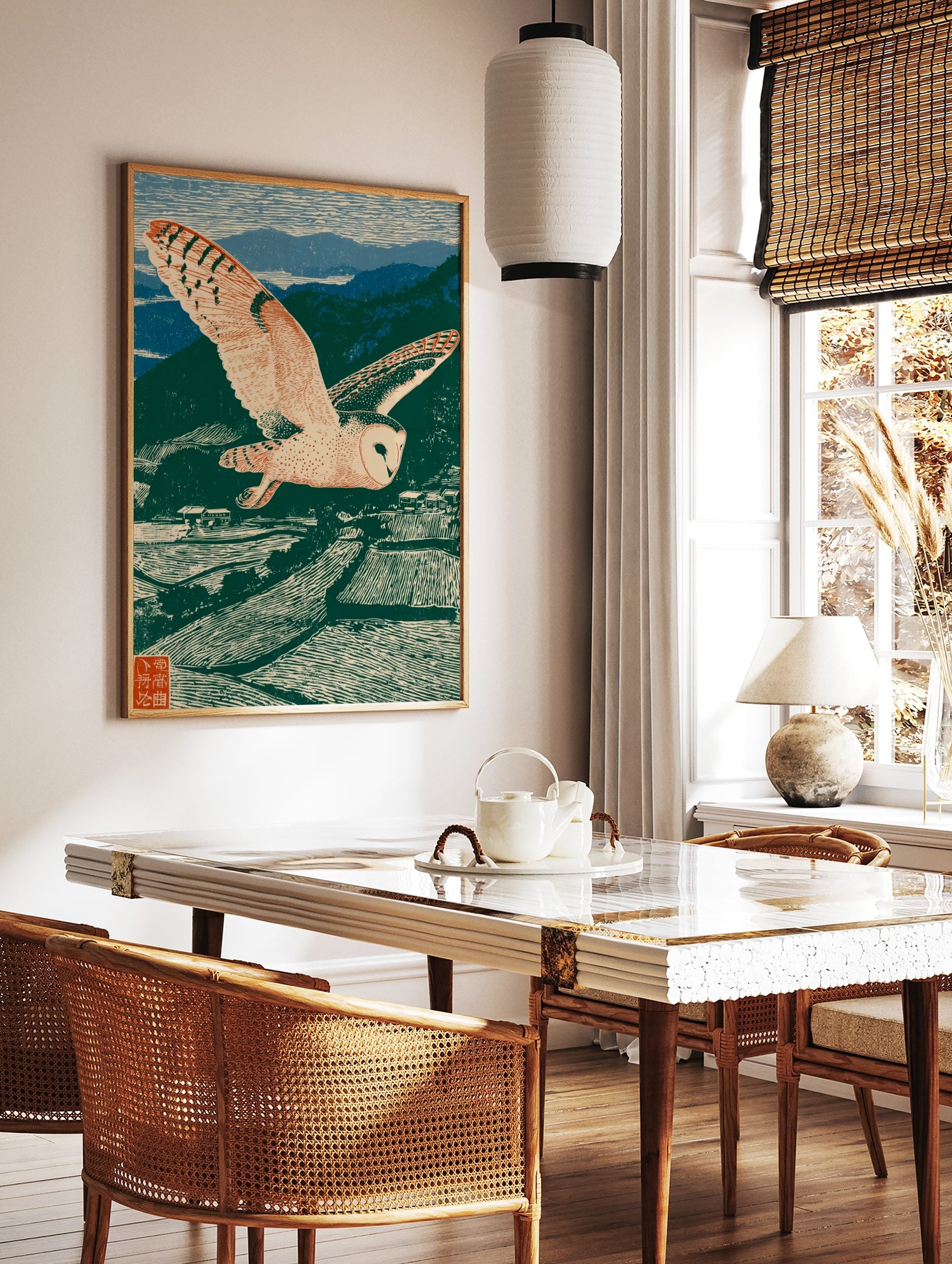 Woodblock style print of a barn owl flying over green terraced fields and blue mountains under a, in a styled room mockup