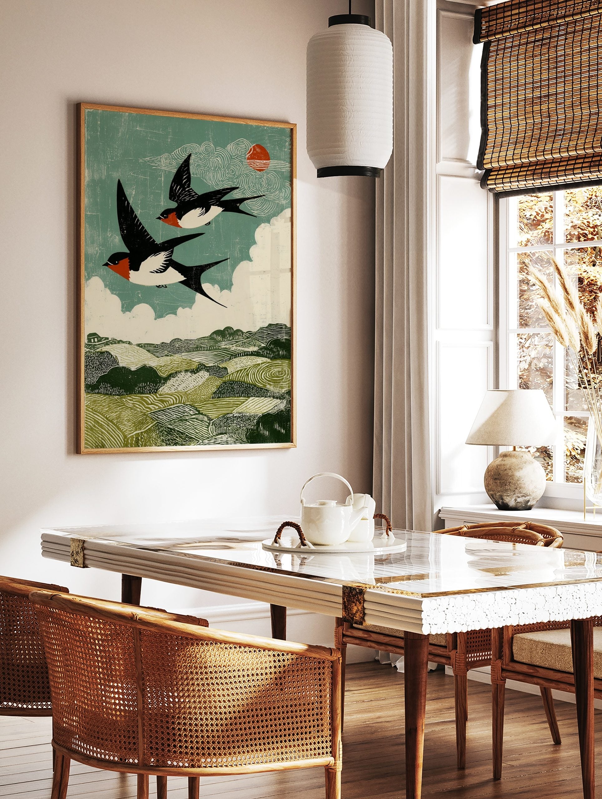 Two barn swallows flying over green hills under a teal sky with white clouds and red sun in woodcut, in a styled room mockup