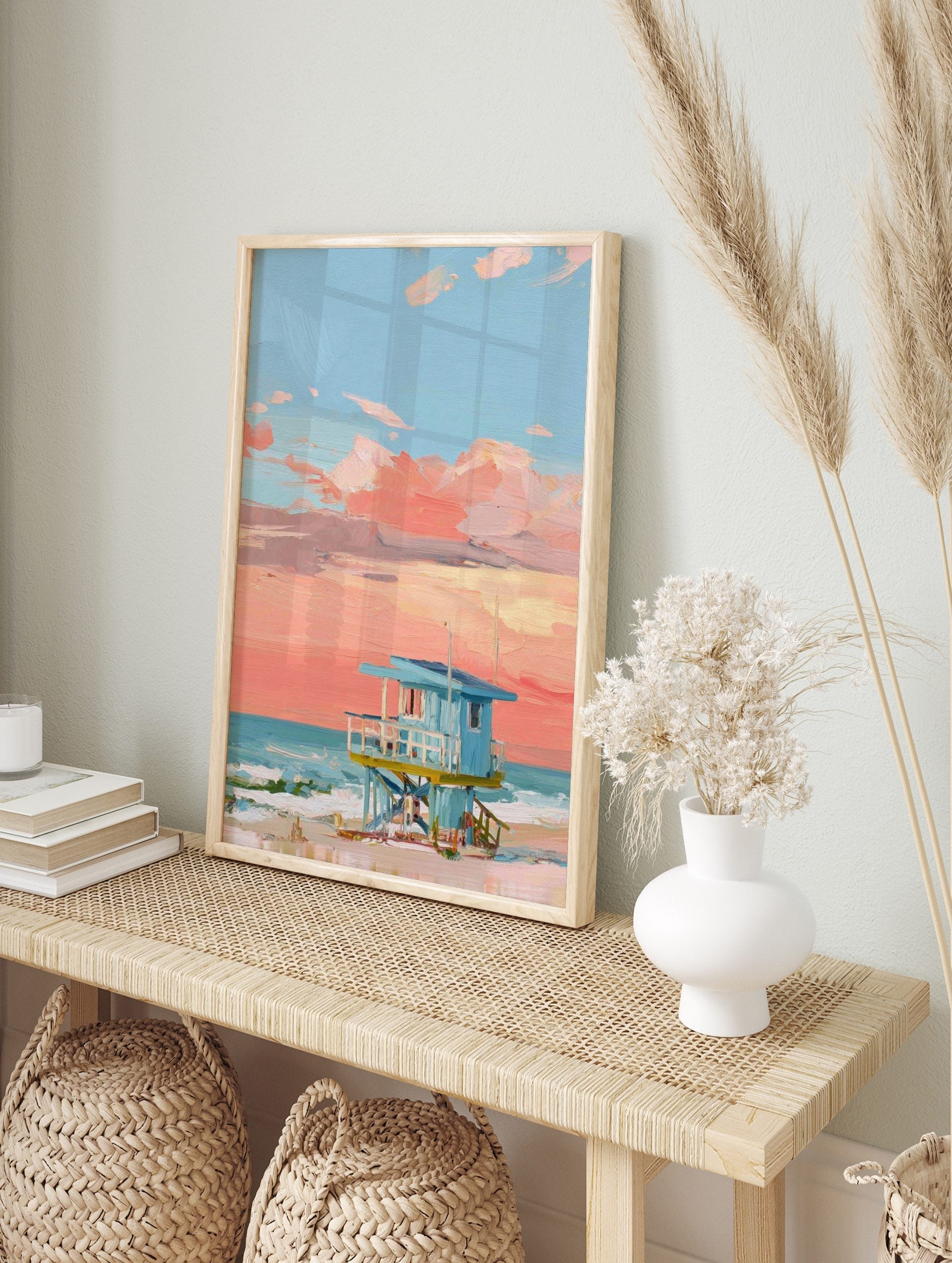 Painted lifeguard hut on a beach with a coral pink and blue sunset sky and ocean waves, in an alternate framed mockup