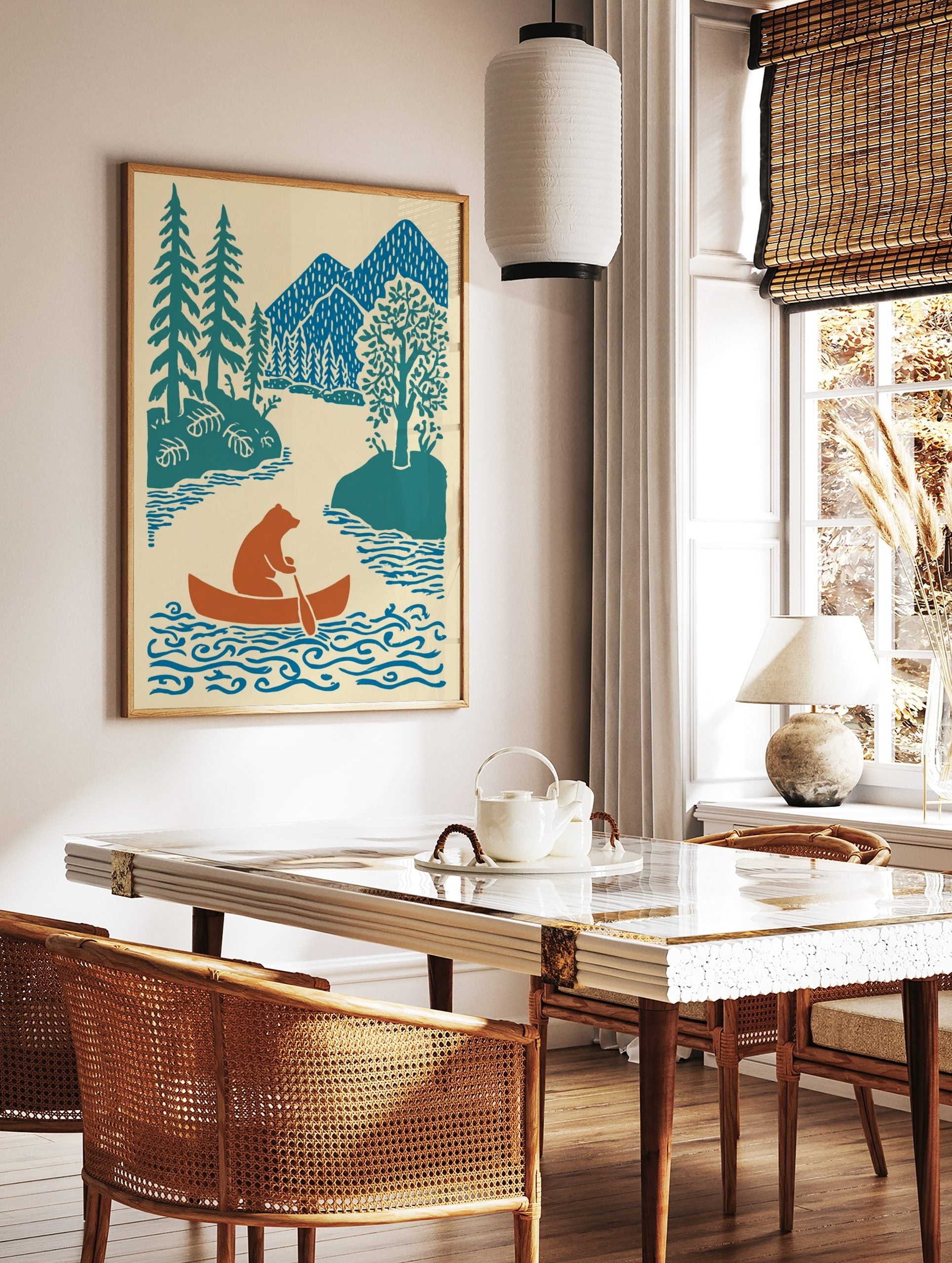 Brown bear paddling orange canoe on blue river with teal trees and blue mountains in illustrative, in a styled room mockup