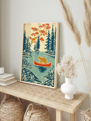 Woodcut style print of a brown bear in a red canoe on a lake, surrounded by blue evergreen, in an alternate framed mockup