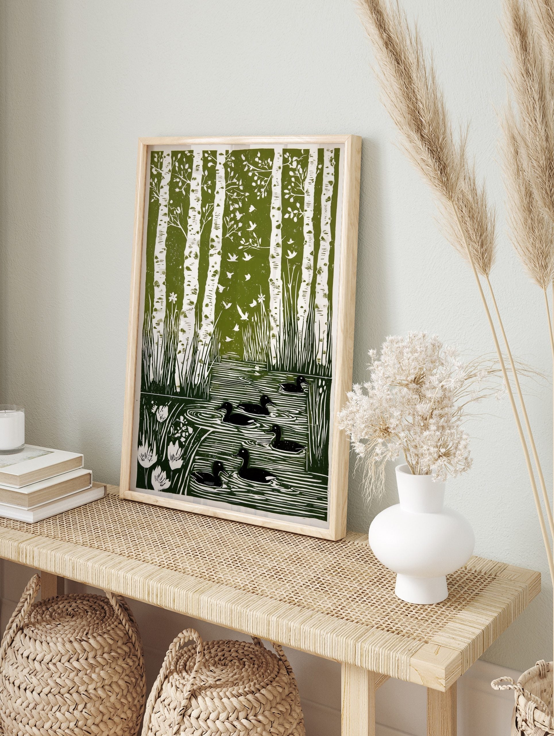 Green and white linocut print of birch trees, flying birds, ducks in a pond, and reeds with, in an alternate framed mockup