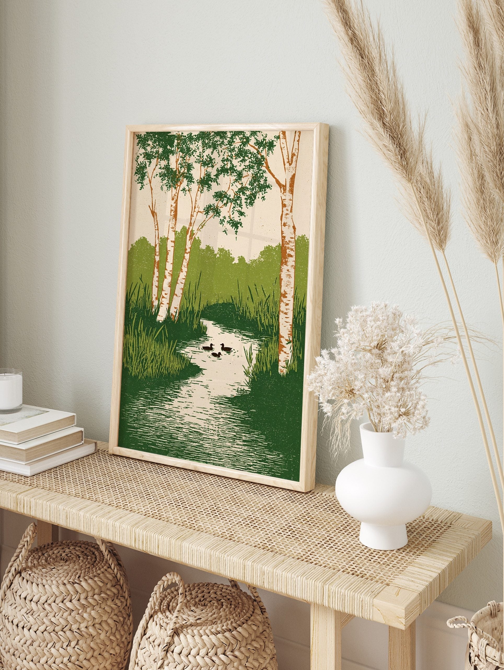 Illustrative wall art of birch trees with green leaves, a winding stream, reeds, and three, in an alternate framed mockup