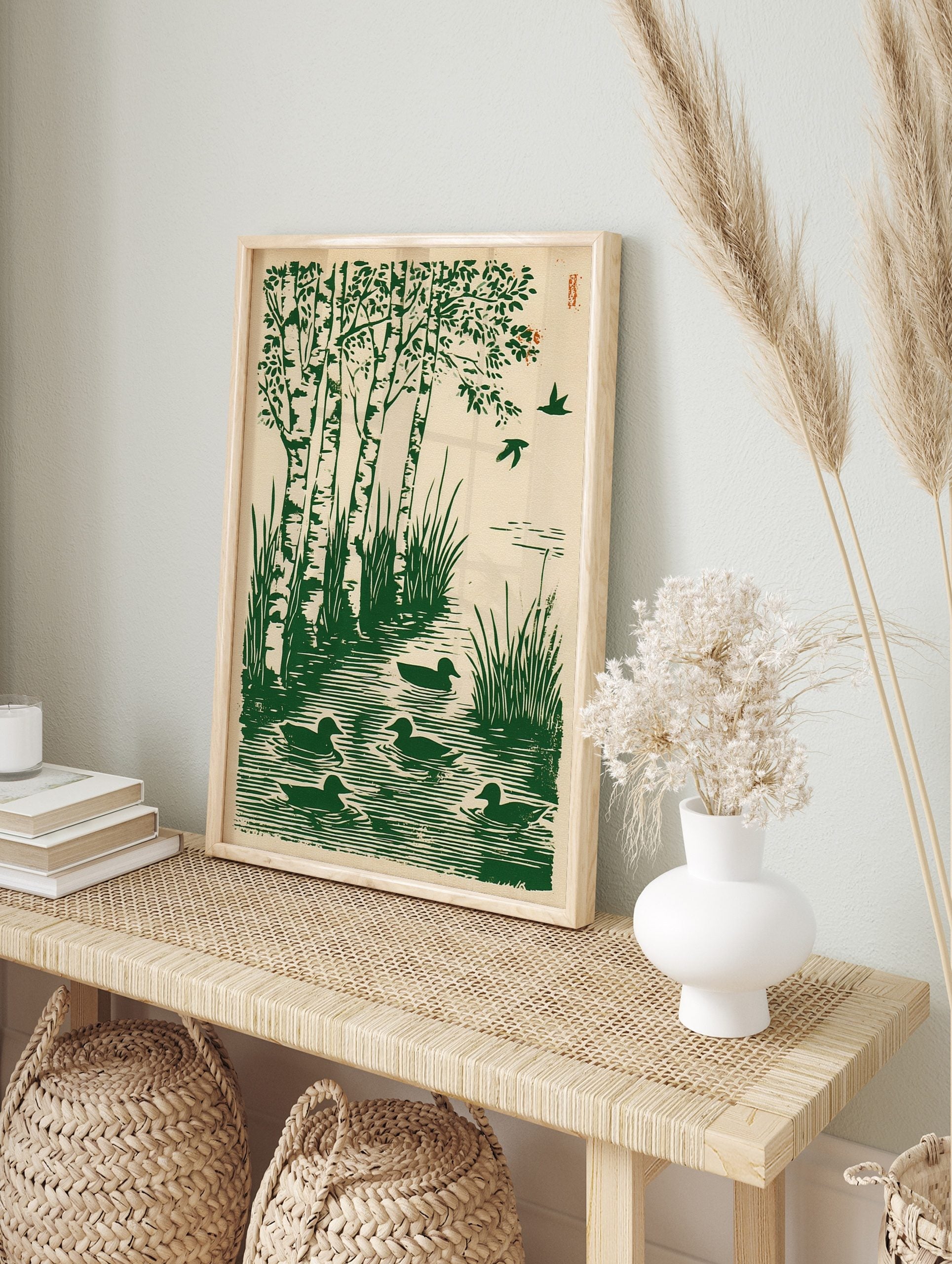 Green woodcut print of birch trees by water with ducks swimming and birds flying, on a beige, in an alternate framed mockup
