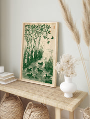 Green woodcut print of birch trees by water with ducks swimming and birds flying, on a beige, in an alternate framed mockup