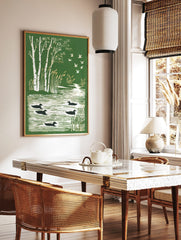 Illustrative print of white birch trees, swimming ducks, and flying geese over a river in green and, in a styled room mockup