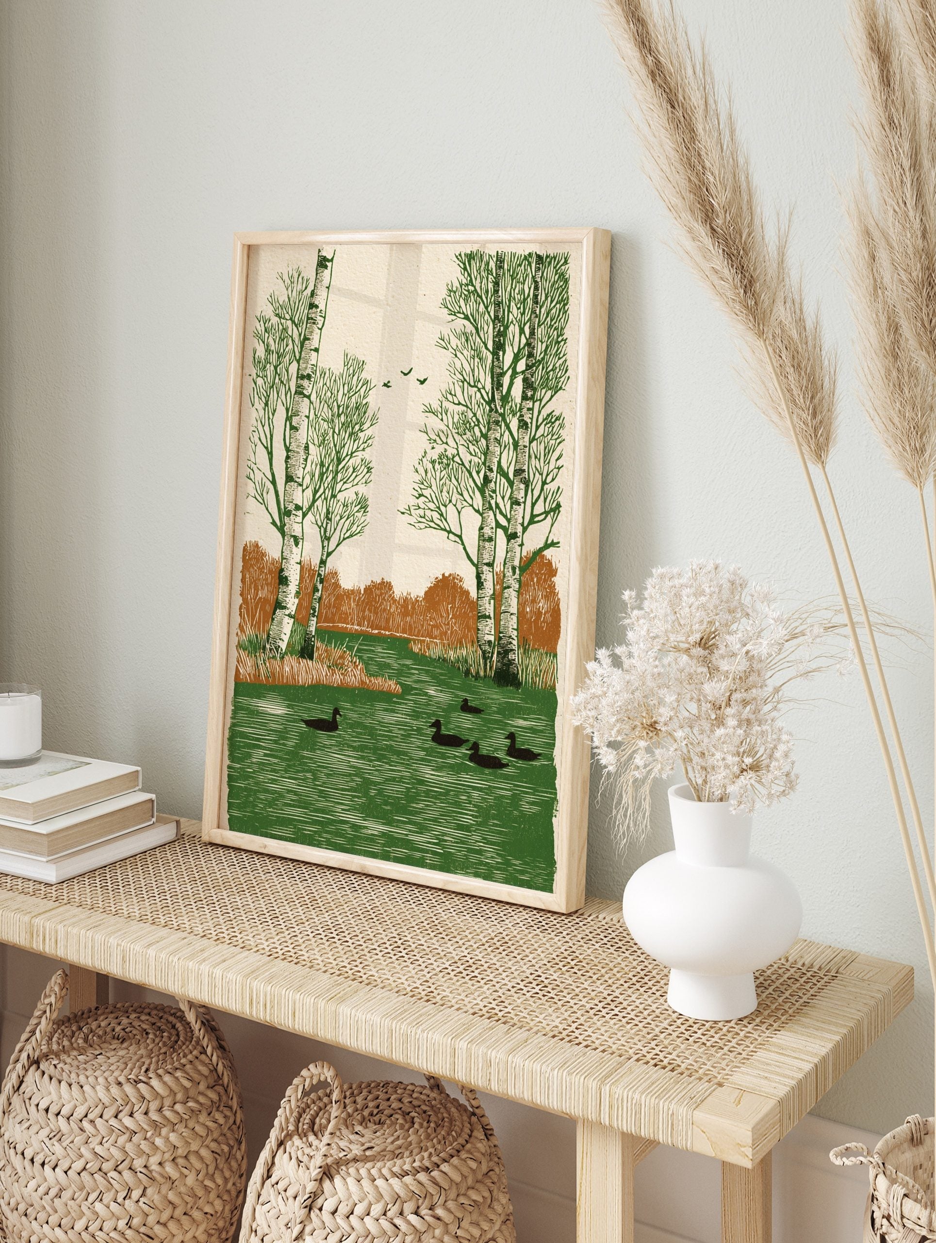 Illustrative print of birch trees, ducks in green water, flying birds, and brown bushes in a, in an alternate framed mockup