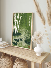 Green woodblock print of white birch trees, weeping leaves, three ducks in a rippling stream, in an alternate framed mockup