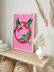 Three stylized birds with green and pink wings flying around a crescent moon inside a red, in an alternate framed mockup
