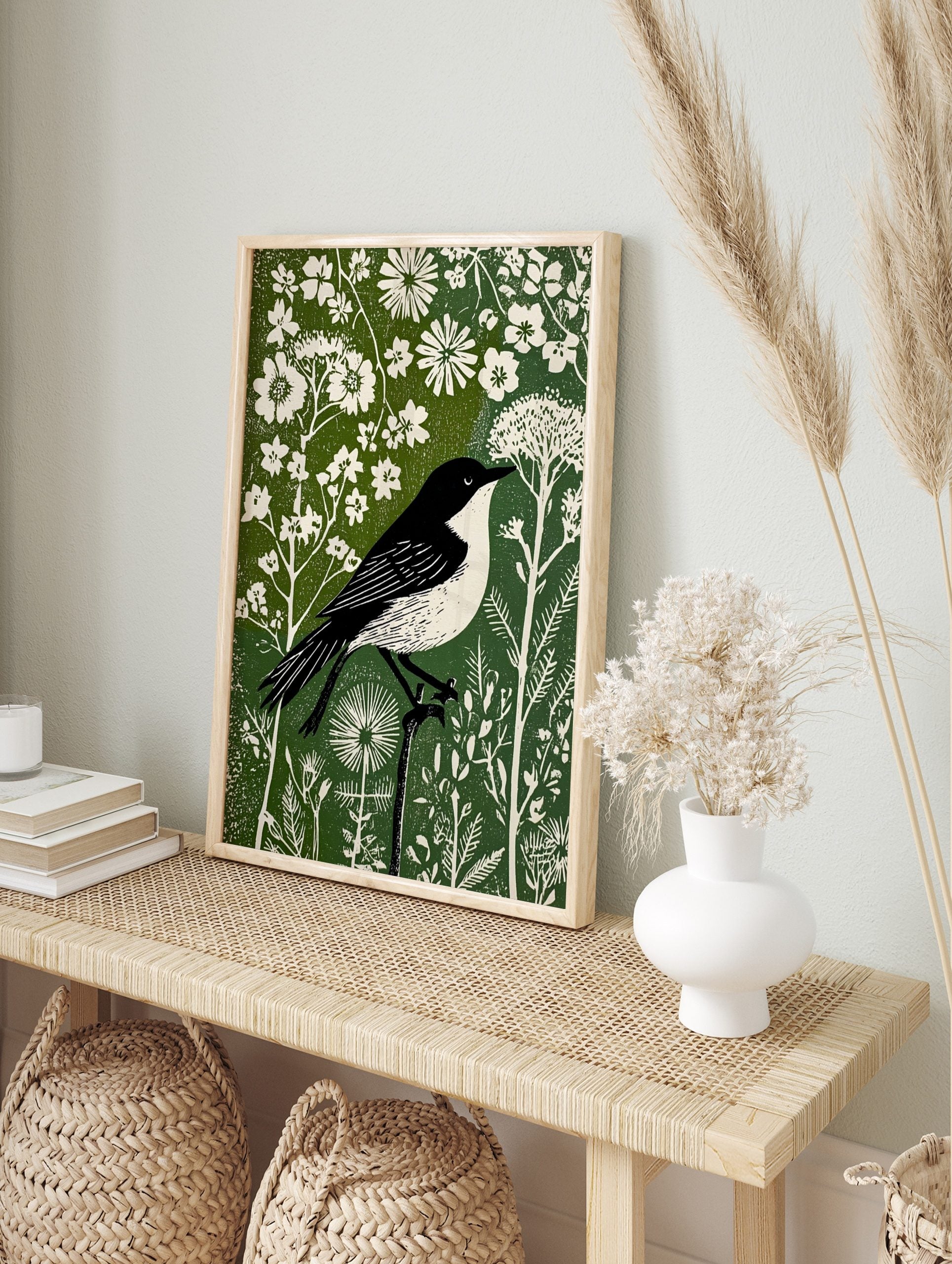 Black and white bird in linocut style perched on branch amidst white flowers and green, in an alternate framed mockup