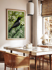 Black bird with white chest and eye on a branch, surrounded by green foliage and white flowers, in a styled room mockup
