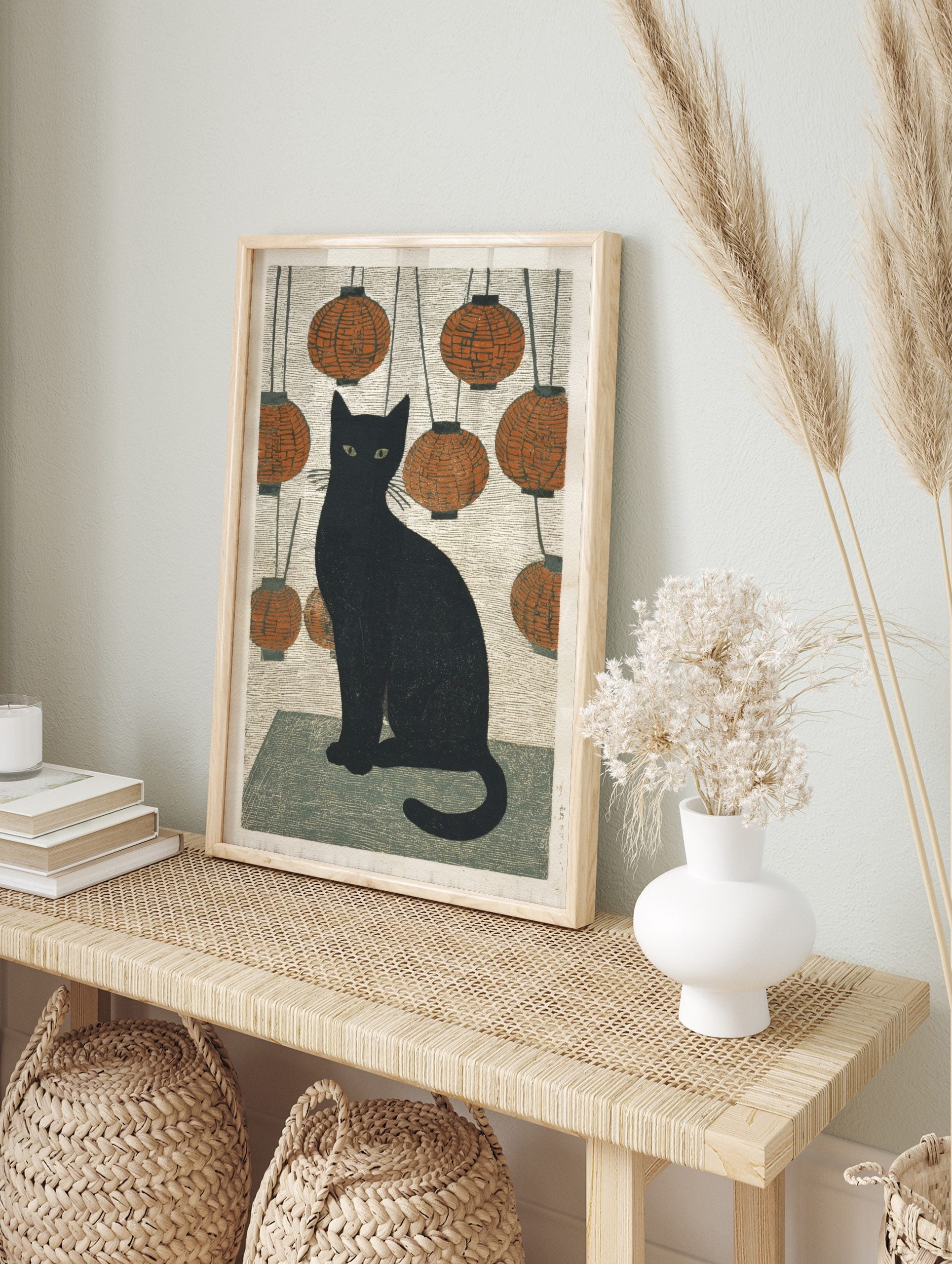 Black cat with green eyes sitting amidst hanging orange lanterns in Japanese woodblock style, in an alternate framed mockup