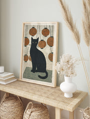 Black cat with green eyes sitting amidst hanging orange lanterns in Japanese woodblock style, in an alternate framed mockup
