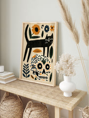 Black cat standing on a floral patterned skull with orange and blue botanical elements on a, in an alternate framed mockup