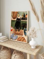Illustration of a black cat wearing oven mitts kneading a loaf of bread on a wooden board in, in an alternate framed mockup