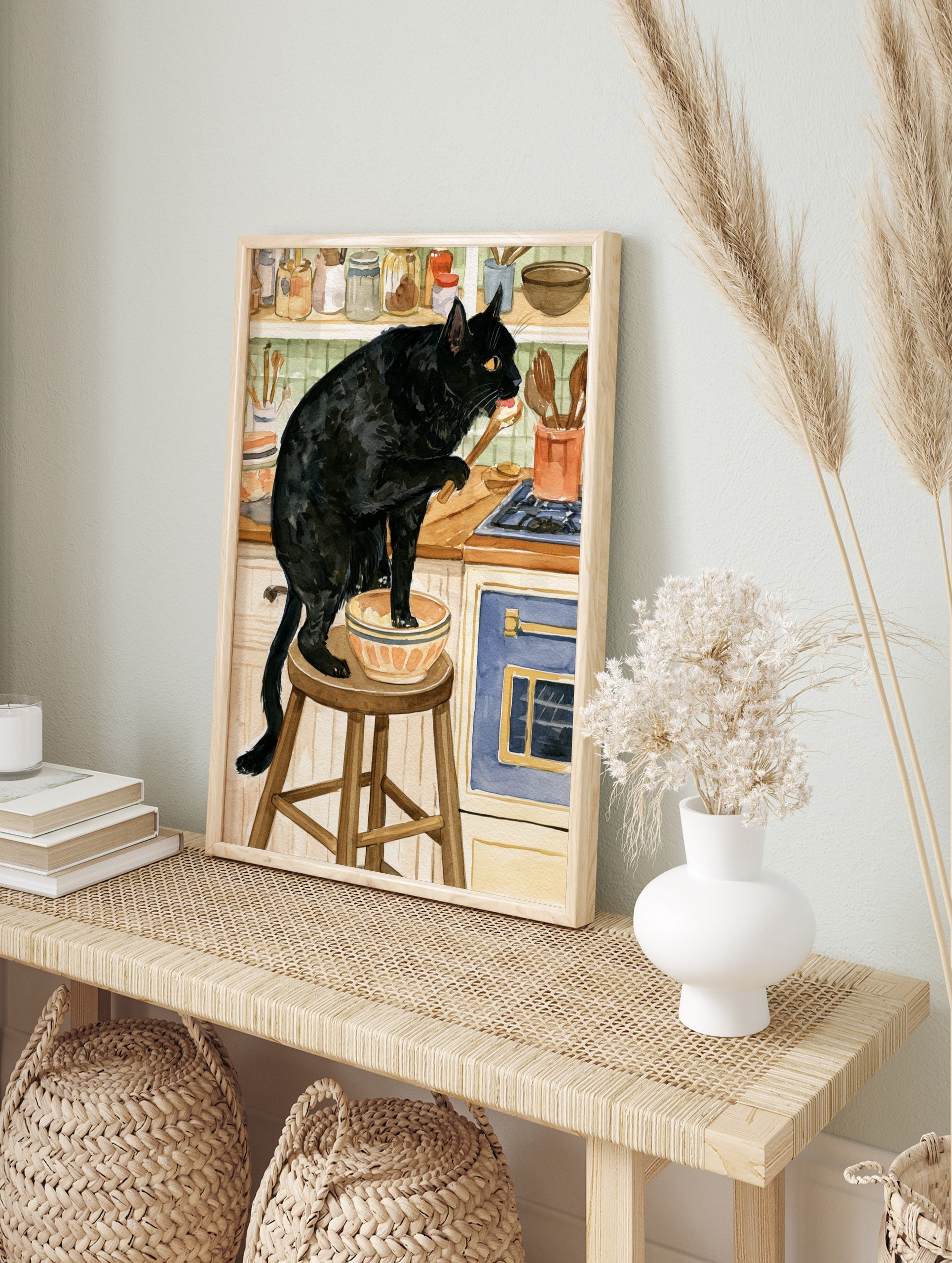Watercolour illustration of a black cat standing on a kitchen stool tasting from a bowl with, in an alternate framed mockup