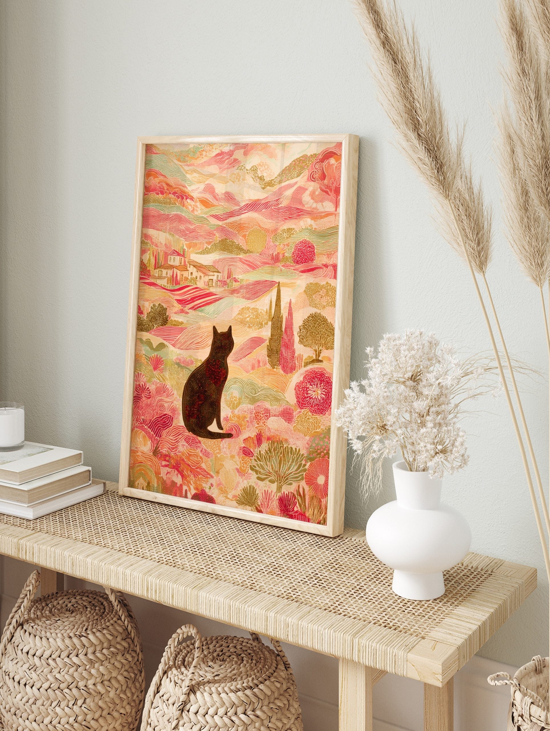 Illustrative print of black cat in colourful landscape with pink hills, green trees, and, in an alternate framed mockup