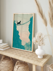 Illustrative print of a black cat walking across a rope bridge between teal cliffs against a, in an alternate framed mockup