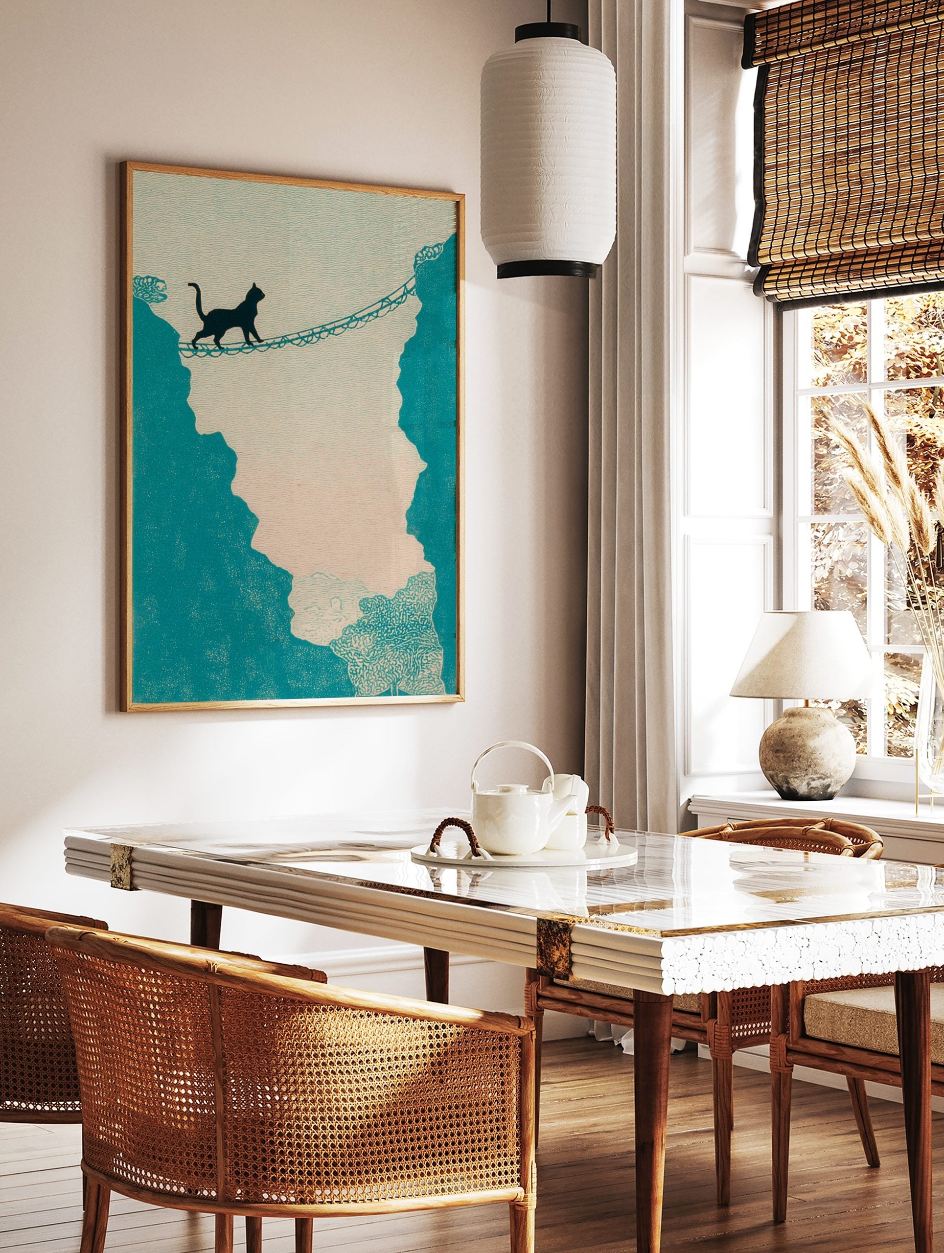 Illustrative print of a black cat walking across a rope bridge between teal cliffs against a light, in a styled room mockup