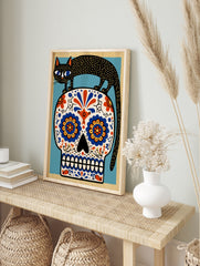 Black cat standing on a decorative sugar skull with vibrant blue and orange floral patterns, in an alternate framed mockup
